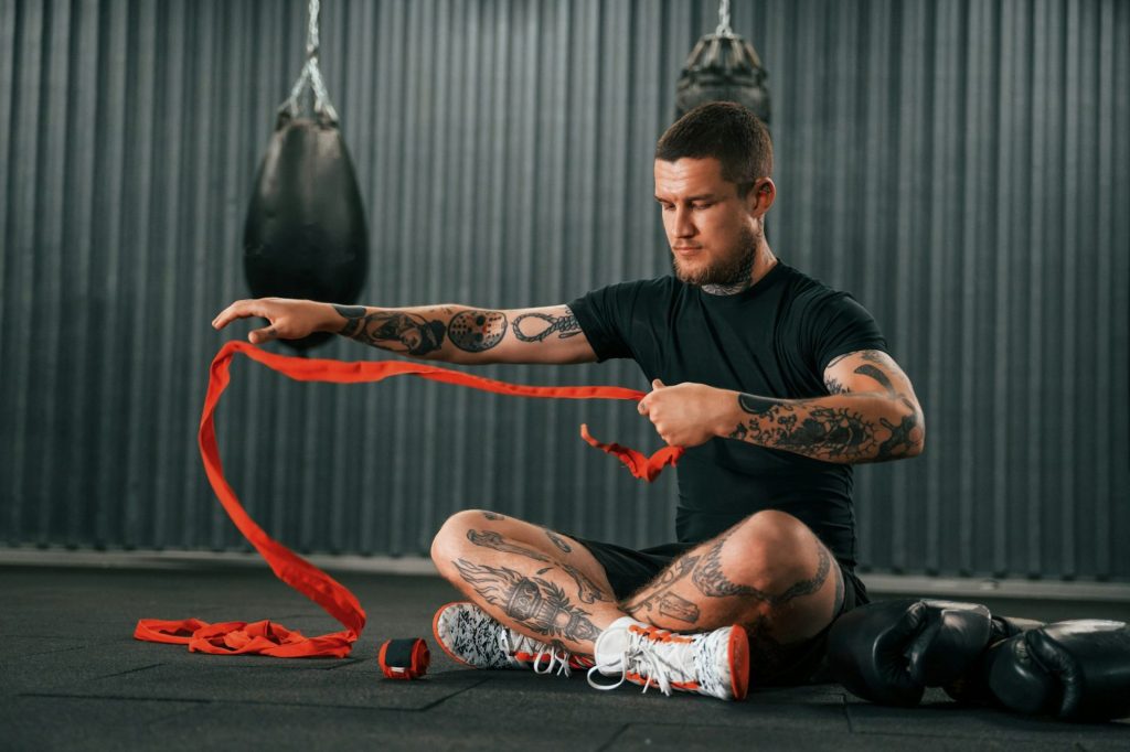 Wearing hand wraps. Young tattooed man is practicing boxing indoors in the gym